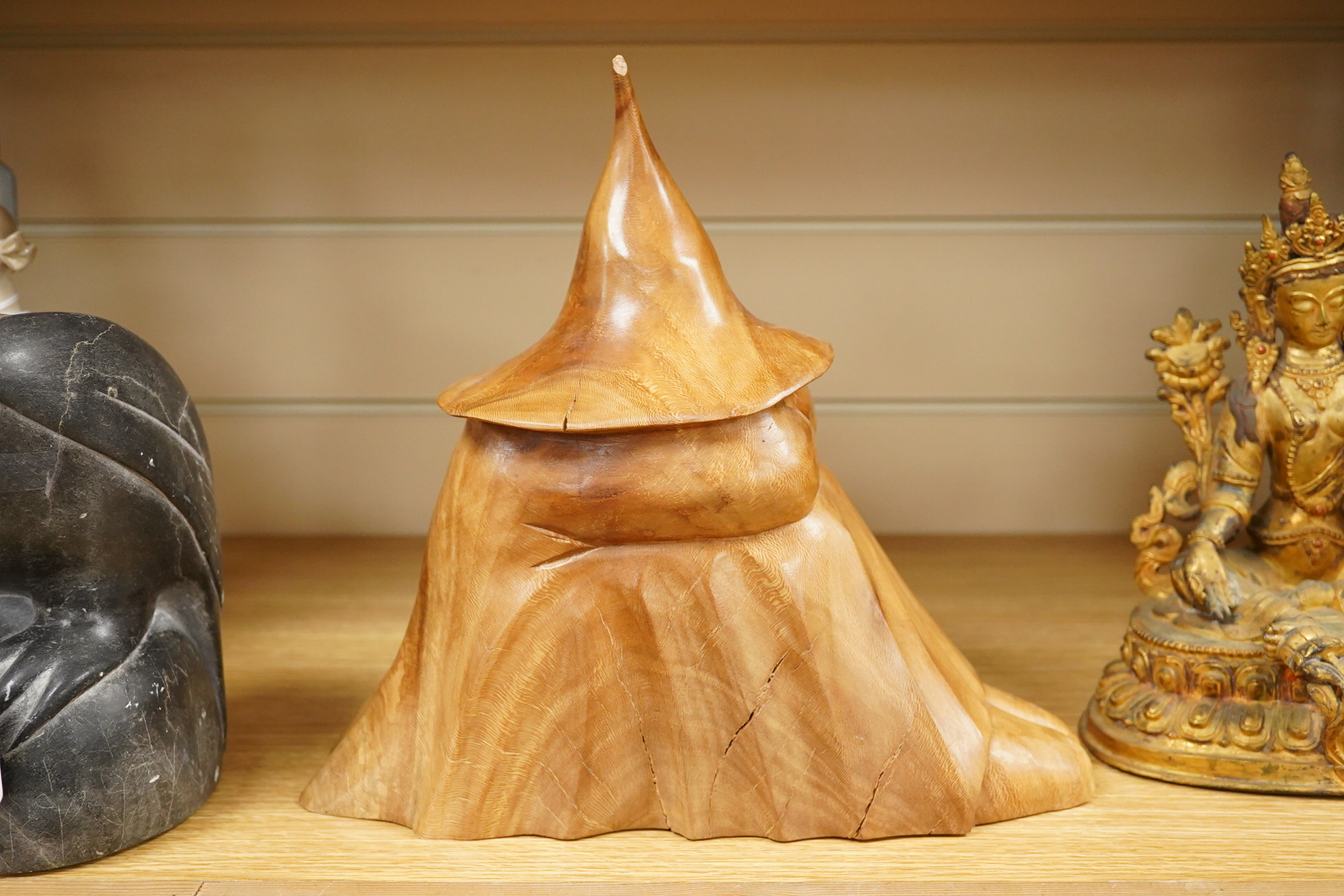 Pierre Decorse (b.1953), a naturalistically modelled wooden sculpture depicting a crouched figure obscured by a large hat 25cm high